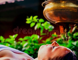 Woman lying with eyes closed as warm oil streams from a brass vessel onto her forehead during an Ayurvedic shirodhara treatment