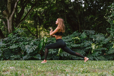 Woman in black activewear holding a lunge pose barefoot on a lawn surrounded by lush tropical plants Woman in black activewear holding a lunge pose barefoot on a lawn surrounded by lush tropical plants