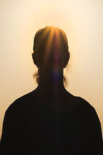 Silhouette of a woman’s head and shoulders with golden sunlight and rainbow light rays streaming through her against a warm, hazy sky Silhouette of a woman’s head and shoulders with golden sunlight and rainbow light rays streaming through her against a warm, hazy sky