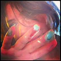 Close-up of a woman peeking through paint-covered fingers smeared with orange, red and turquoise Close-up of a woman peeking through paint-covered fingers smeared with orange, red and turquoise