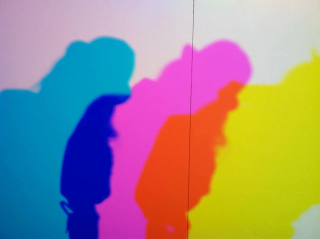 Overlapping colorful shadows in turquoise, blue, magenta, orange and yellow cast by a person on a white wall Overlapping colorful shadows in turquoise, blue, magenta, orange and yellow cast by a person on a white wall