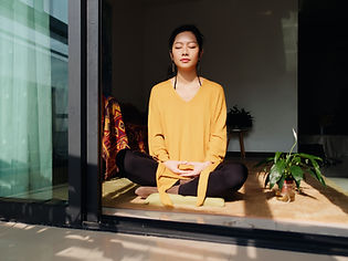 Woman in a mustard sweater meditating cross-legged with eyes closed in a sunlit doorway beside a potted plant Woman in a mustard sweater meditating cross-legged with eyes closed in a sunlit doorway beside a potted plant