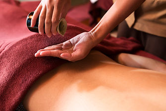 Massage therapist pouring warm oil onto her hand before an Ayurvedic oil massage on a client’s back Massage therapist pouring warm oil onto her hand before an Ayurvedic oil massage on a client’s back