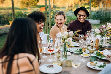 Group of friends laughing together around an outdoor dinner table in a garden, set with wine glasses, small plates and wildflowers Group of friends laughing together around an outdoor dinner table in a garden, set with wine glasses, small plates and wildflowers