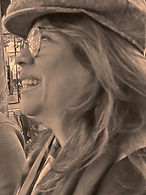 Sepia-toned photo of a smiling woman with long hair, glasses and a newsboy cap, laughing outdoors Sepia-toned photo of a smiling woman with long hair, glasses and a newsboy cap, laughing outdoors