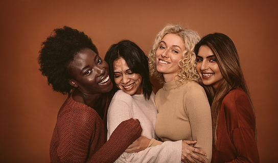 Four smiling women of different backgrounds hugging closely in cozy sweaters against a warm terracotta backdrop Four smiling women of different backgrounds hugging closely in cozy sweaters against a warm terracotta backdrop