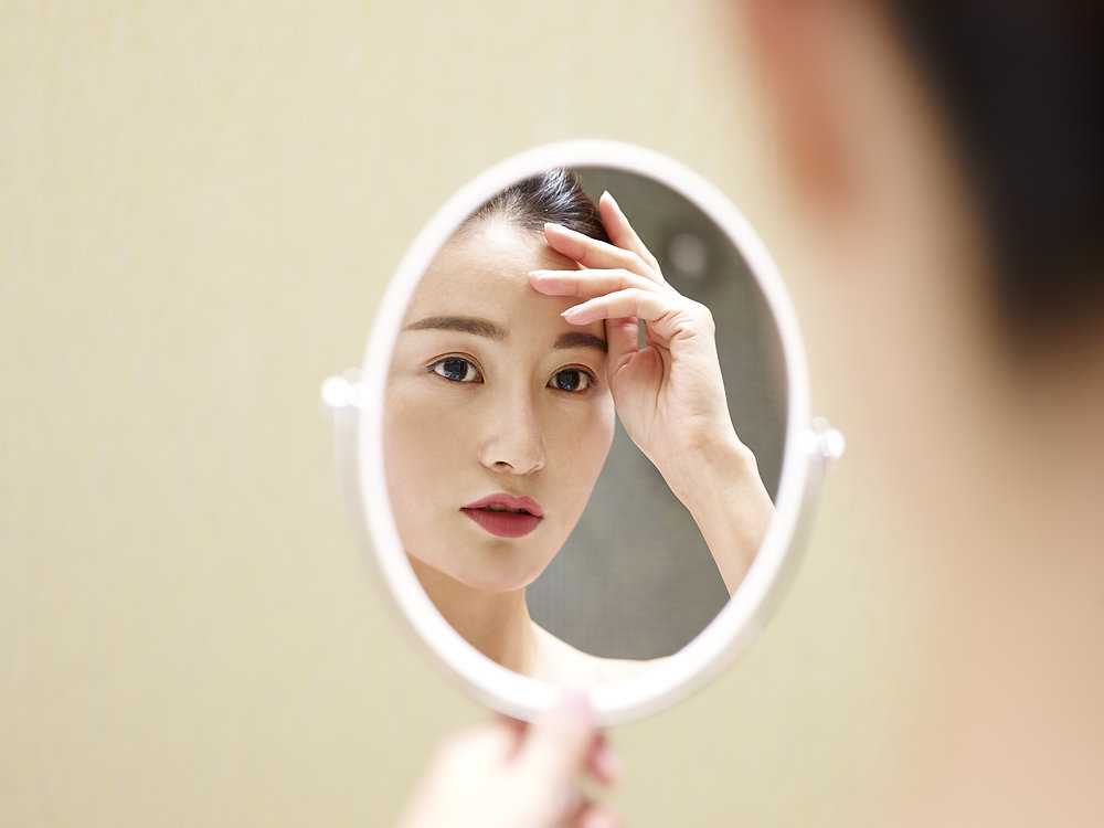 Woman with dark hair and red lips gazing at her reflection in a small handheld oval mirror Woman with dark hair and red lips gazing at her reflection in a small handheld oval mirror