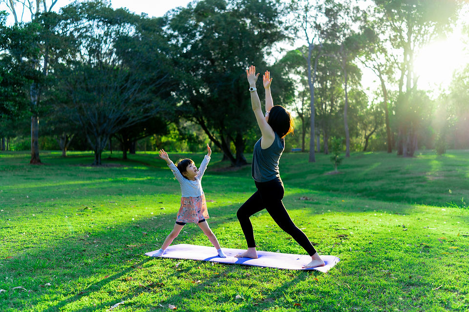 Mother and young daughter doing yoga together on a mat in a sunlit park, both reaching their arms up to the sky Mother and young daughter doing yoga together on a mat in a sunlit park, both reaching their arms up to the sky