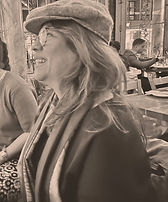 Sepia-toned photo of a smiling woman with long hair in glasses and a newsboy cap, enjoying time out at a lively café Sepia-toned photo of a smiling woman with long hair in glasses and a newsboy cap, enjoying time out at a lively café