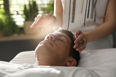 Man lying relaxed with eyes closed on a white treatment table while a reiki practitioner holds a hand on his head and a crystal pendulum above him Man lying relaxed with eyes closed on a white treatment table while a reiki practitioner holds a hand on his head and a crystal pendulum above him