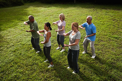 Group of adults practicing tai chi together on a green lawn, arms extended in the same slow pose Group of adults practicing tai chi together on a green lawn, arms extended in the same slow pose