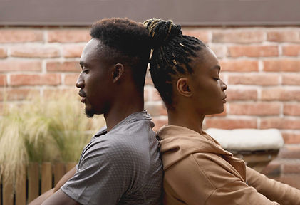 Man and woman sitting back to back with eyes closed, meditating calmly outdoors in front of a red brick wall Man and woman sitting back to back with eyes closed, meditating calmly outdoors in front of a red brick wall