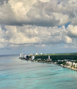 Aerial view of a turquoise sea along a coastline lined with hotels and green trees, under big white clouds Aerial view of a turquoise sea along a coastline lined with hotels and green trees, under big white clouds