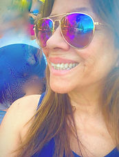 Smiling woman with long brown hair wearing rainbow mirrored aviator sunglasses and a blue top at a sunny outdoor event Smiling woman with long brown hair wearing rainbow mirrored aviator sunglasses and a blue top at a sunny outdoor event