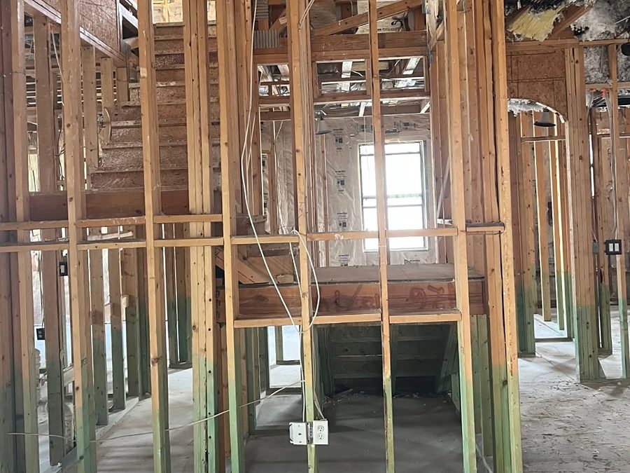 Home interior stripped to bare studs with a green band on the lower framing, open stair framing and insulation hanging from the ceiling