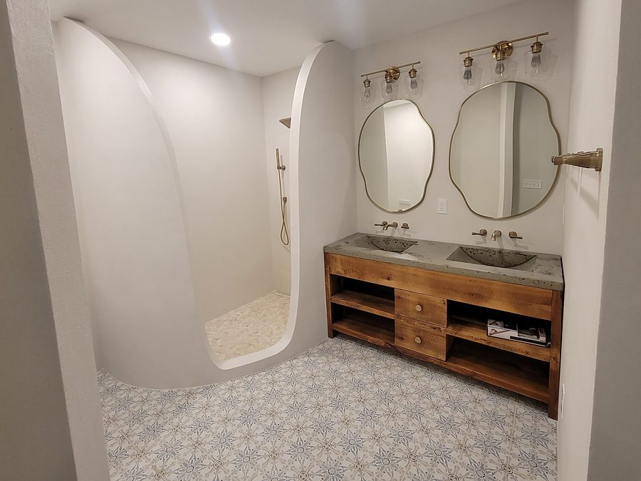 Bathroom by Onsite Construction with a curved plaster walk in shower, wood double vanity, organic shaped mirrors and patterned floor tile