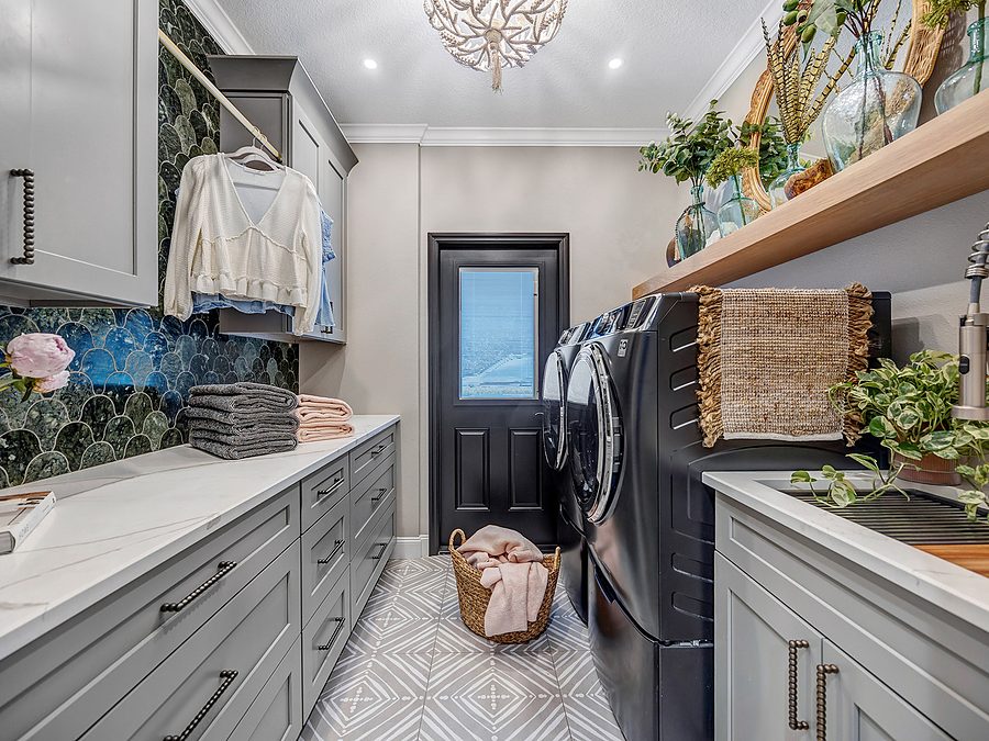 Laundry room by Onsite Construction with gray shaker cabinets, green scale tile, a white quartz counter, washer and dryer and a patterned tile floor