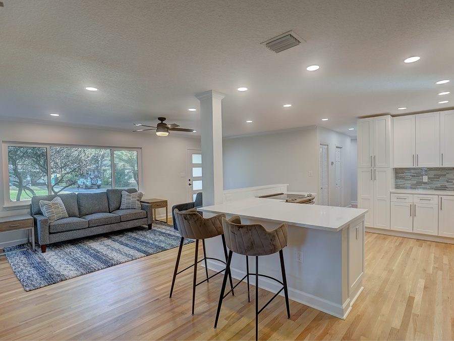 Open plan living room and kitchen with white shaker cabinets, a peninsula with stools, recessed lights and light oak floor