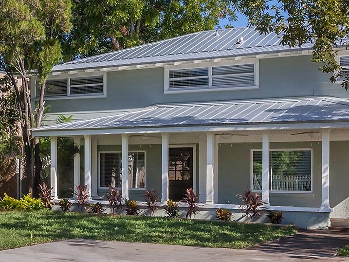 Two story blue gray home by Onsite Construction with a long white porch, metal roof and banded windows