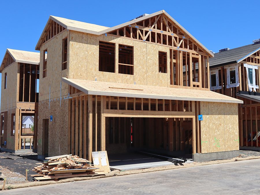 Two story new house framed in wood with OSB sheathing and an open garage bay, with scrap lumber stacked at the curb