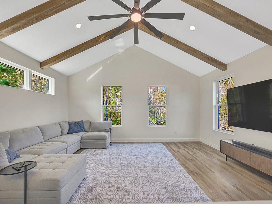 Upstairs bonus room by Onsite Construction with a vaulted ceiling, exposed wood beams, gray sectional and large windows
