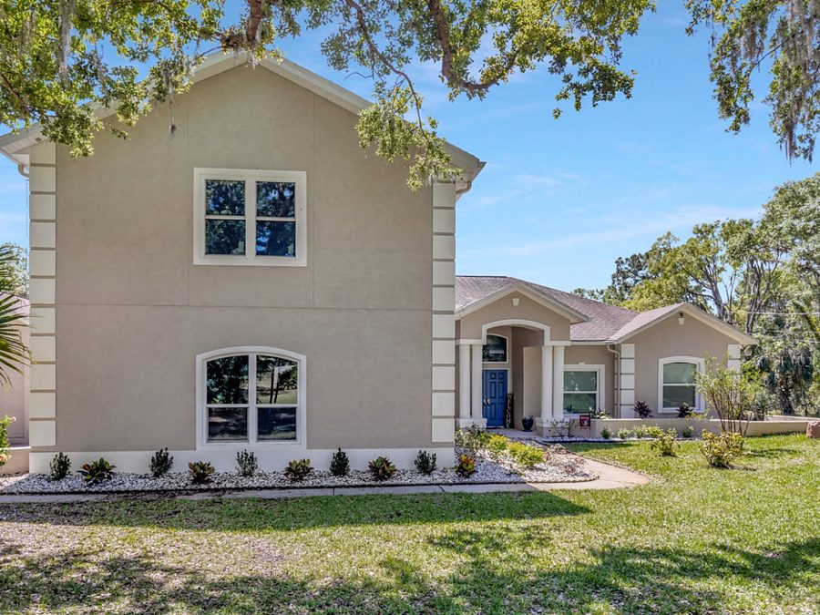 Two story tan stucco section with quoin corners and an arched window joined to a one story stucco home with an arched entry and blue door