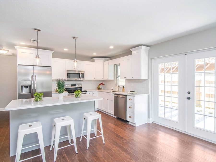 White kitchen by Onsite Construction with a gray island, white stools, stainless appliances and French doors
