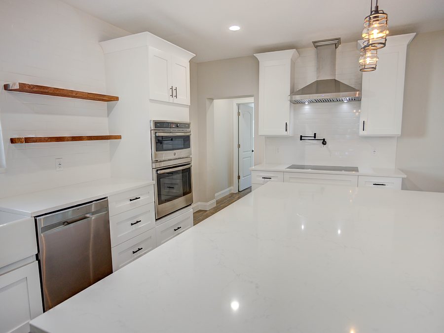 White shaker kitchen with a quartz island, rustic floating shelves, wall ovens and subway tile