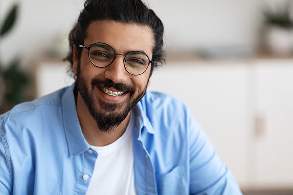 Smiling adult male with dark hair and glasses, with braces on his teeth