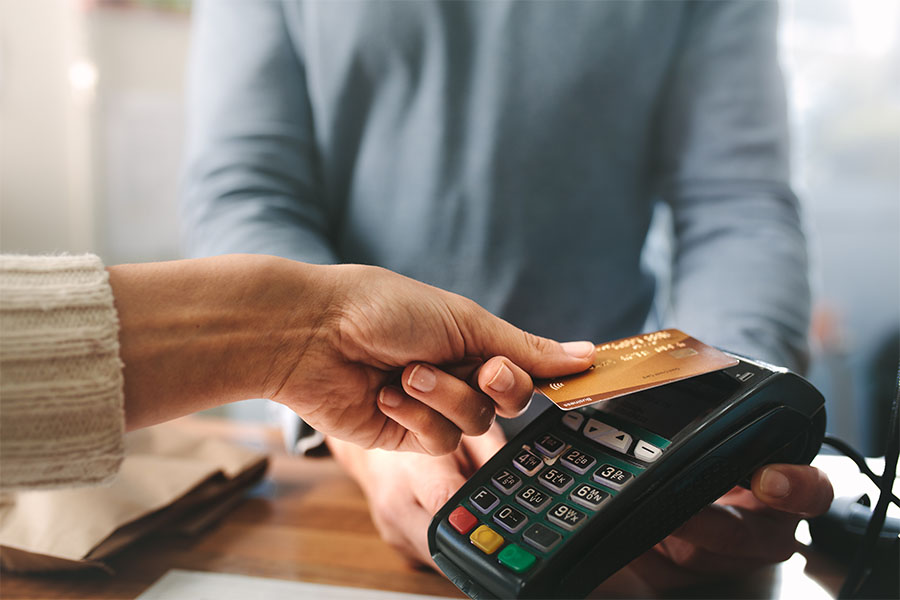 Close up of a woman holding her credit card up to the credit card terminal a man wearing a grey shirt is holding