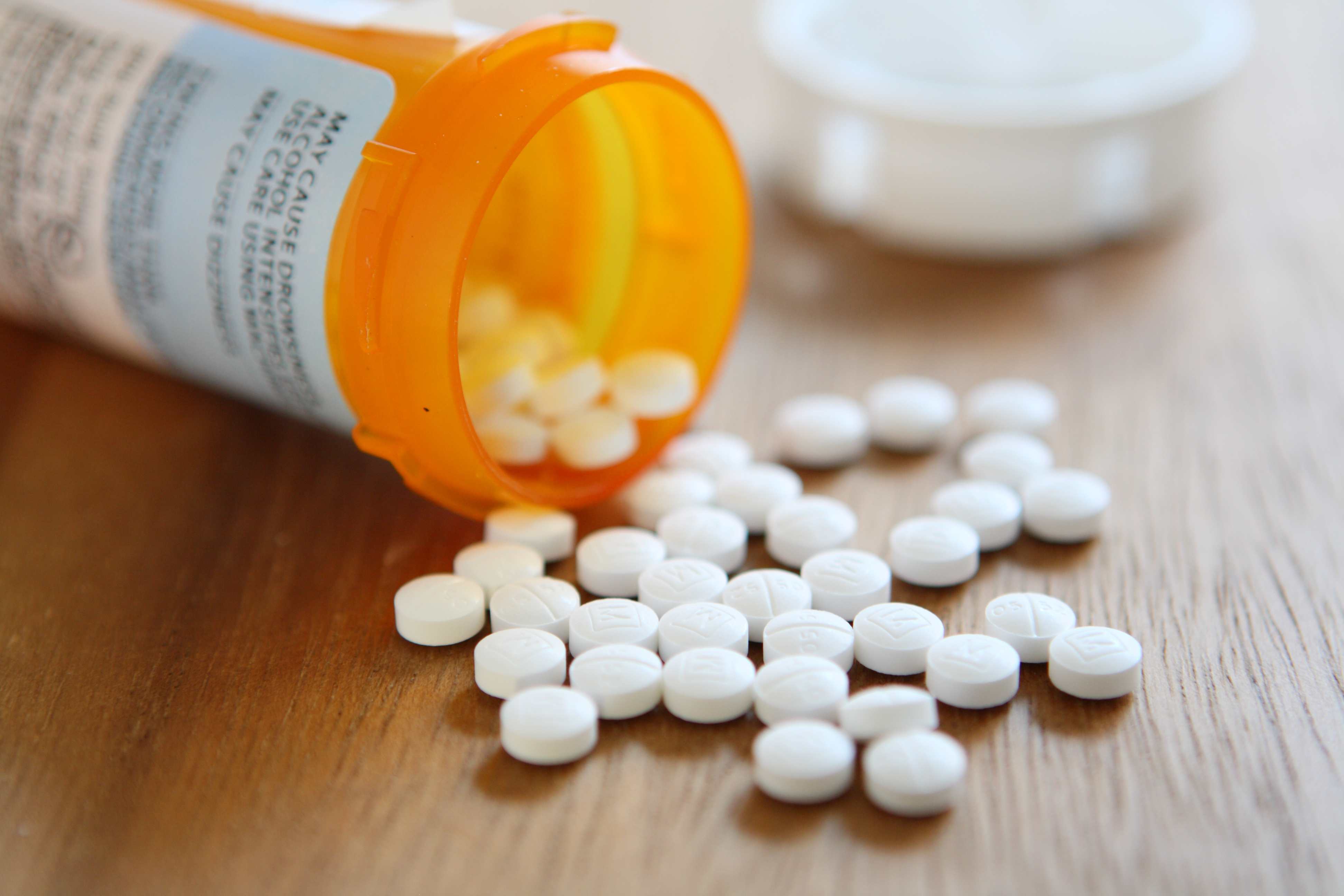 Prescription pill bottle open with white pills coming out on table