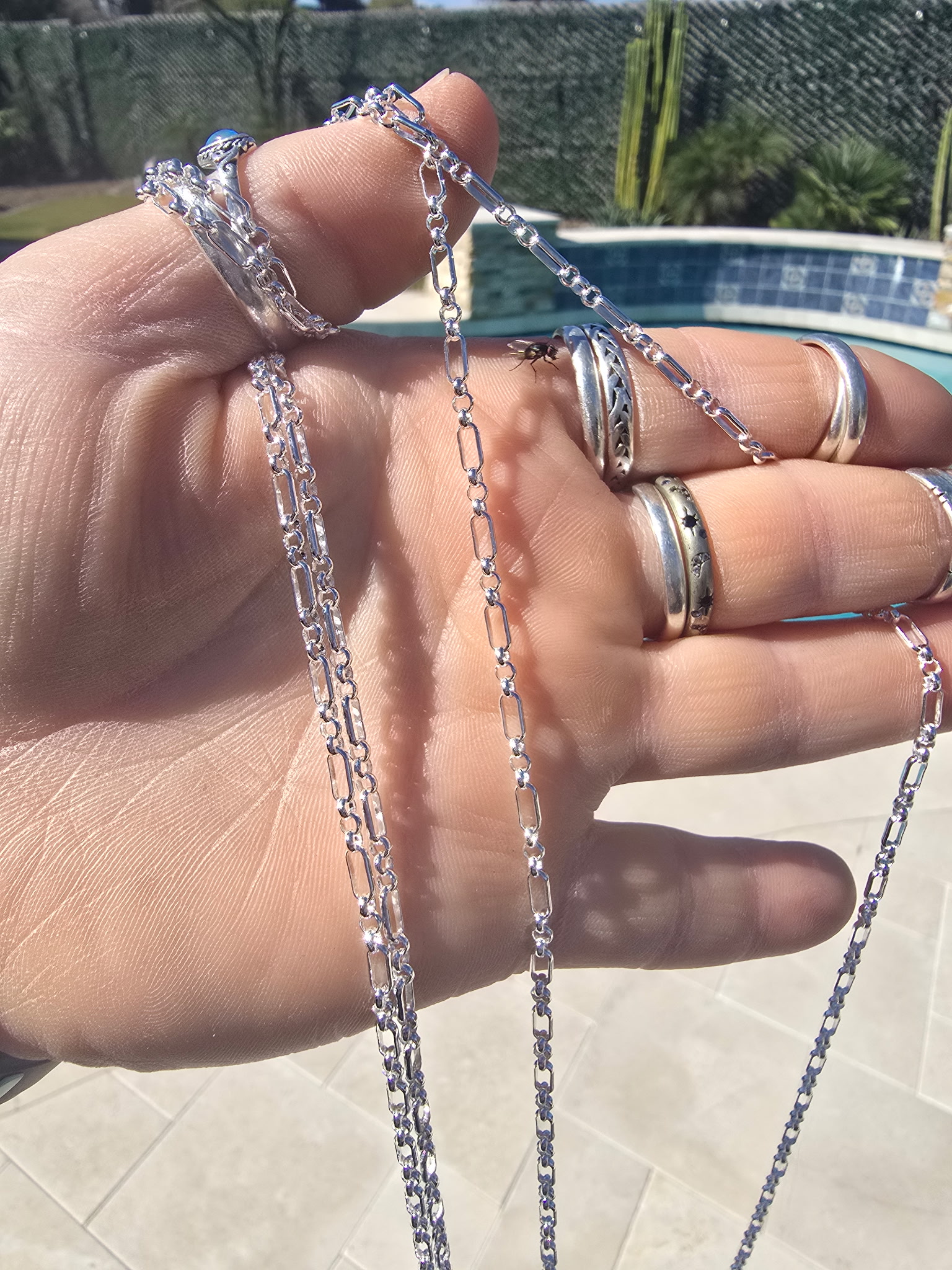 Hand holding gold and silver permanent chain samples poolside during a mobile fitting