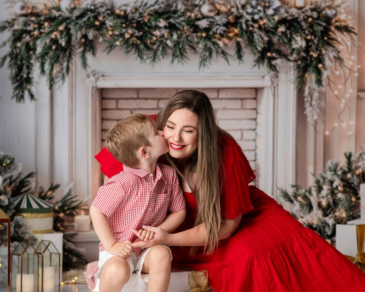 Family of four posing together in a festive Christmas studio with a decorated fireplace and Christmas trees.