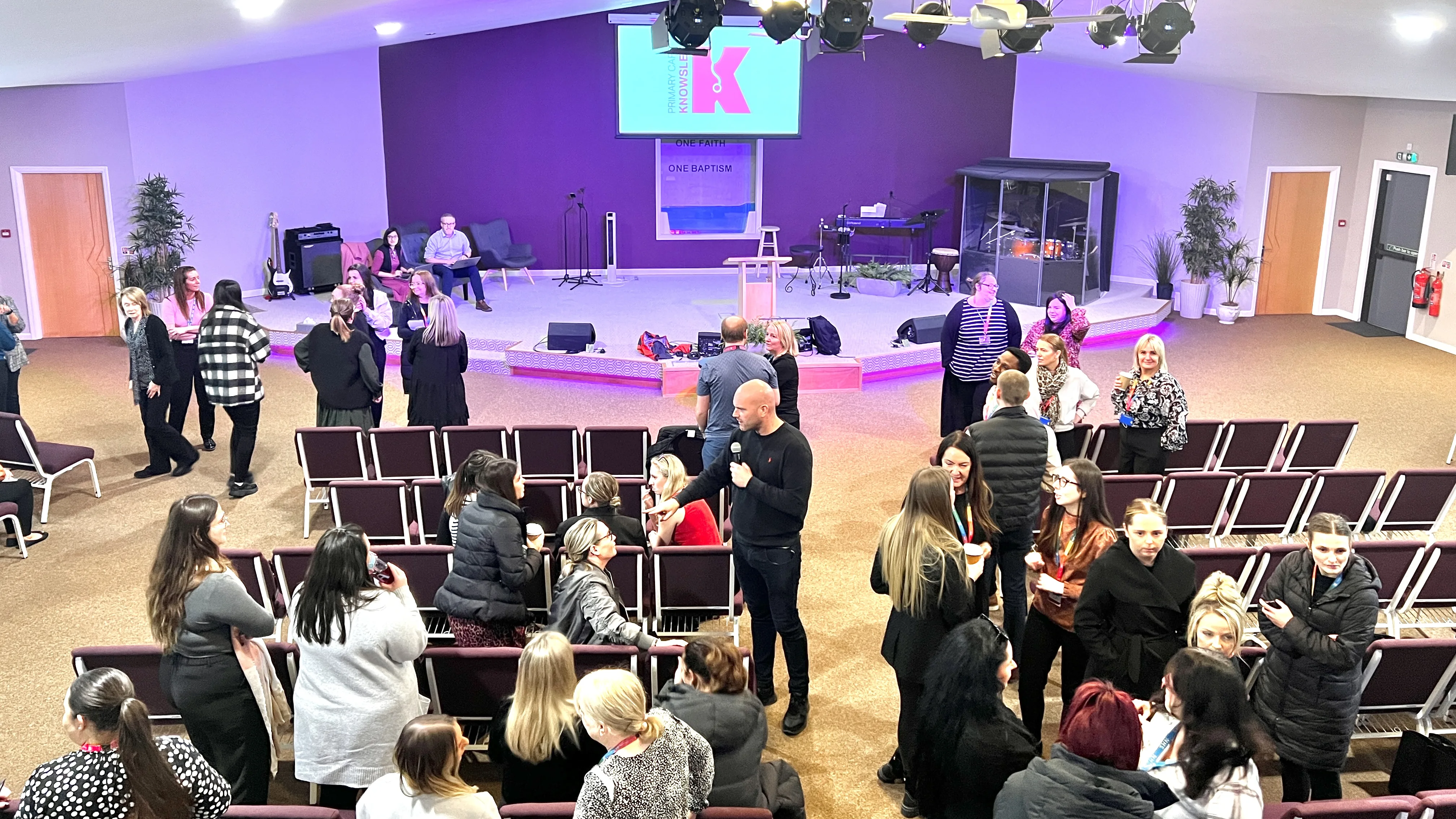 A busy event in the Auditorium at the Maggie O'Neill Centre, with purple stage lighting
