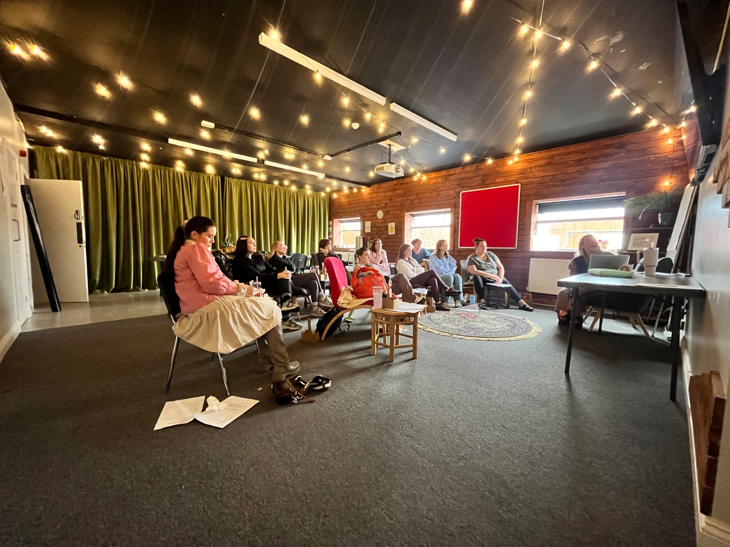 Nursery staff training in the Community Room at the Maggie O'Neill Centre, sitting in a circle under festoon lights
