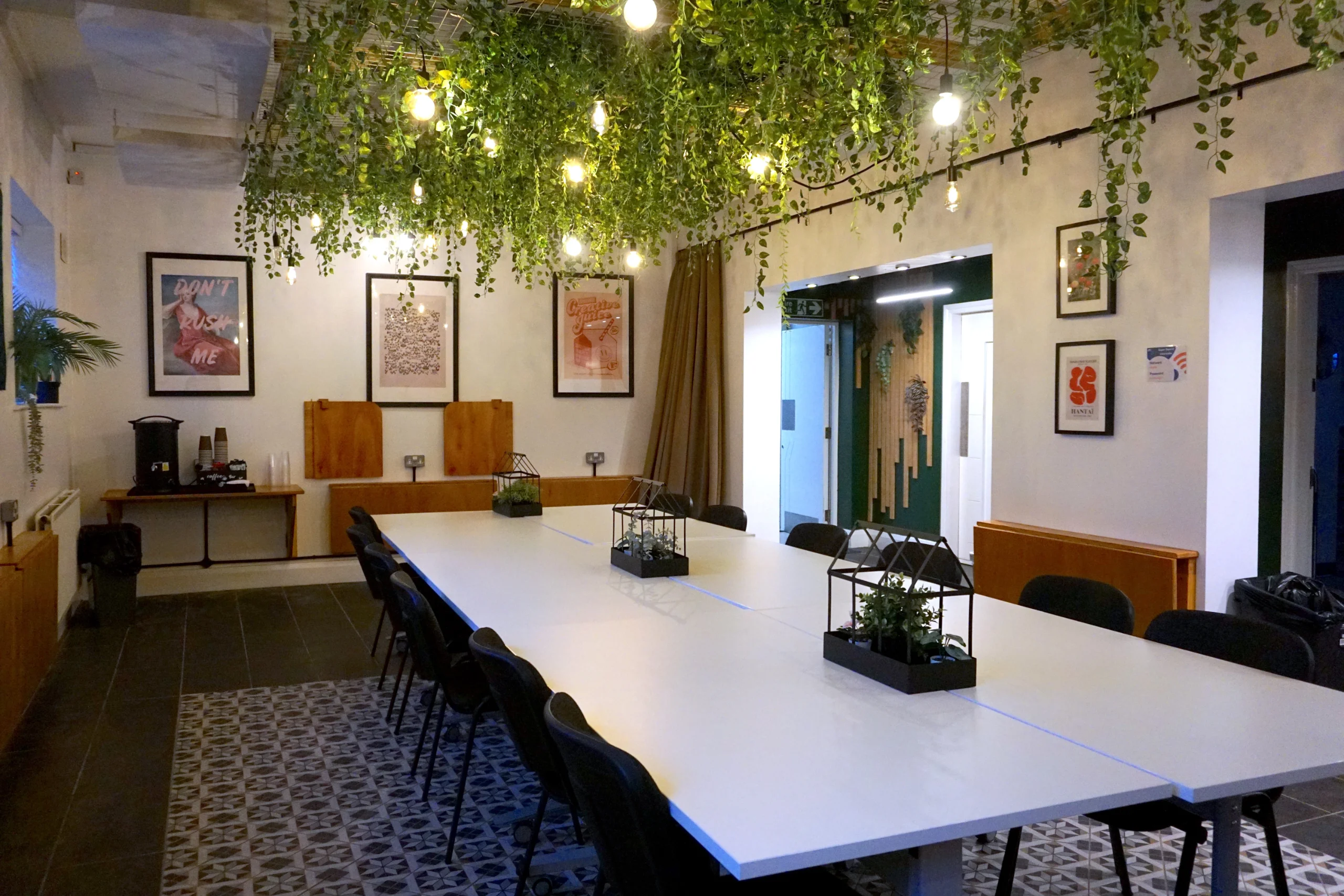 The Grove meeting room at the Maggie O'Neill Centre, looking along the table past the prints to the doorway, under the greenery canopy