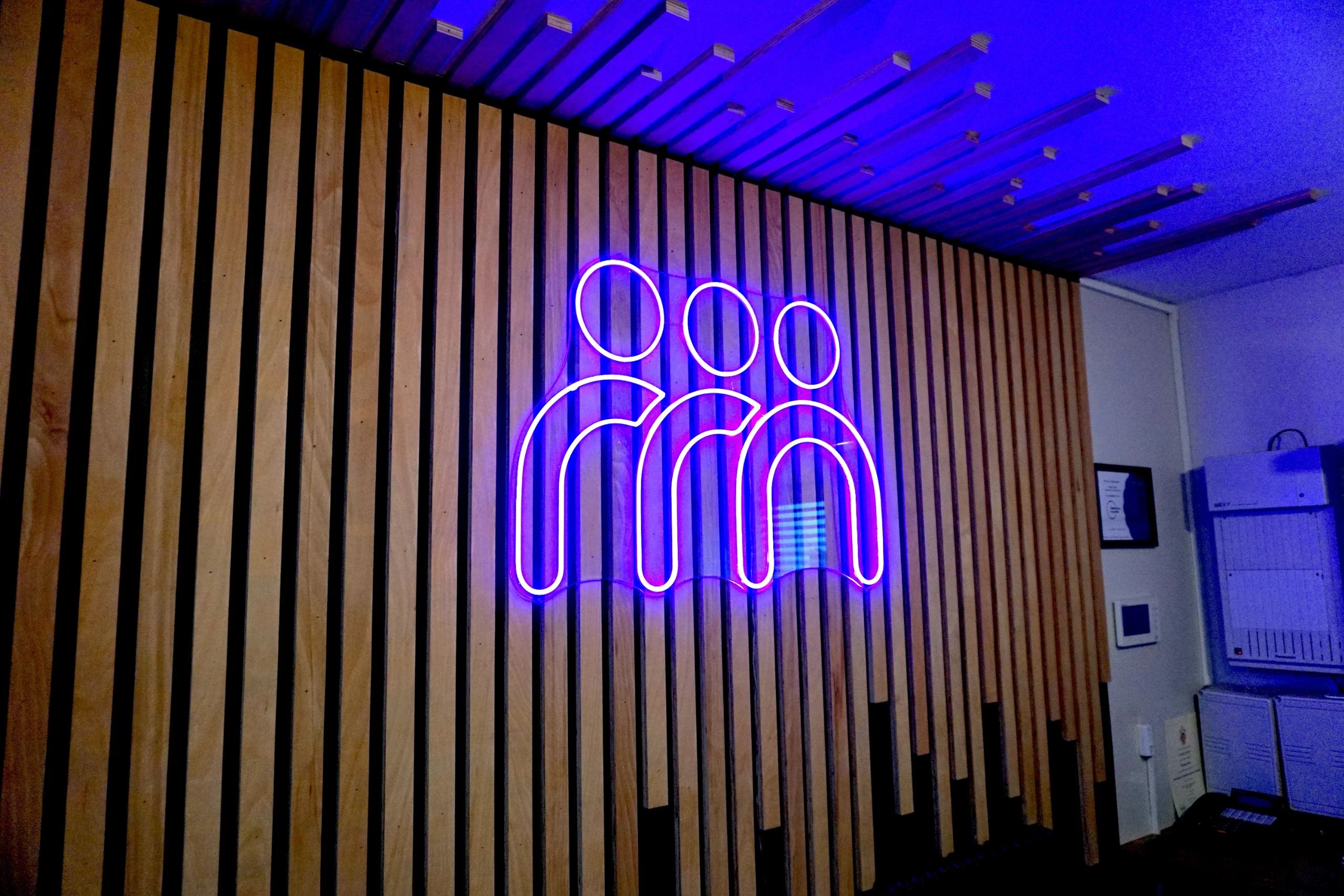 The purple neon logo on the oak slat wall in reception at the Maggie O'Neill Centre
