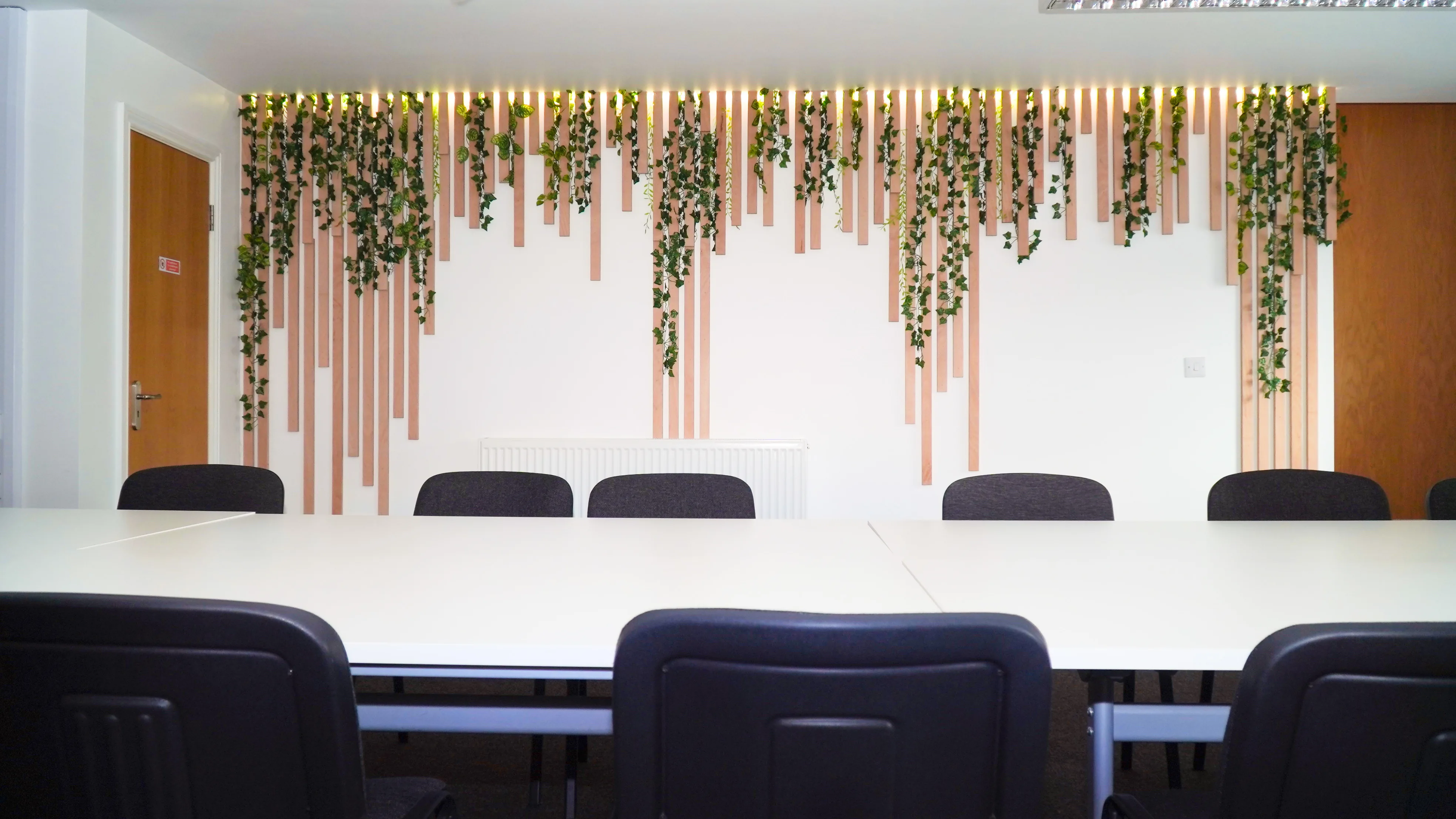The Forum at the Maggie O'Neill Centre, with a long white table in front of the greenery-draped oak slat wall and warm lights
