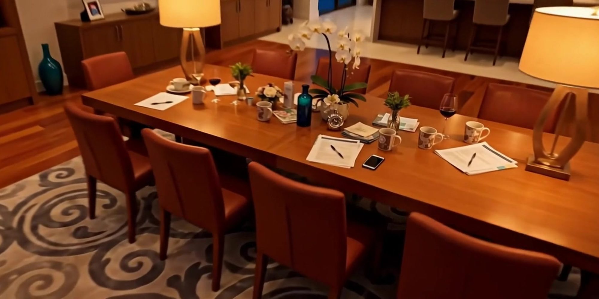 A dining table at night with papers, coffee cups and a phone, under warm lamps.