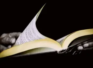 A hand gently turning the page of a book, soft natural lighting, quiet moment captured in close-up, calm reflective atmosphere