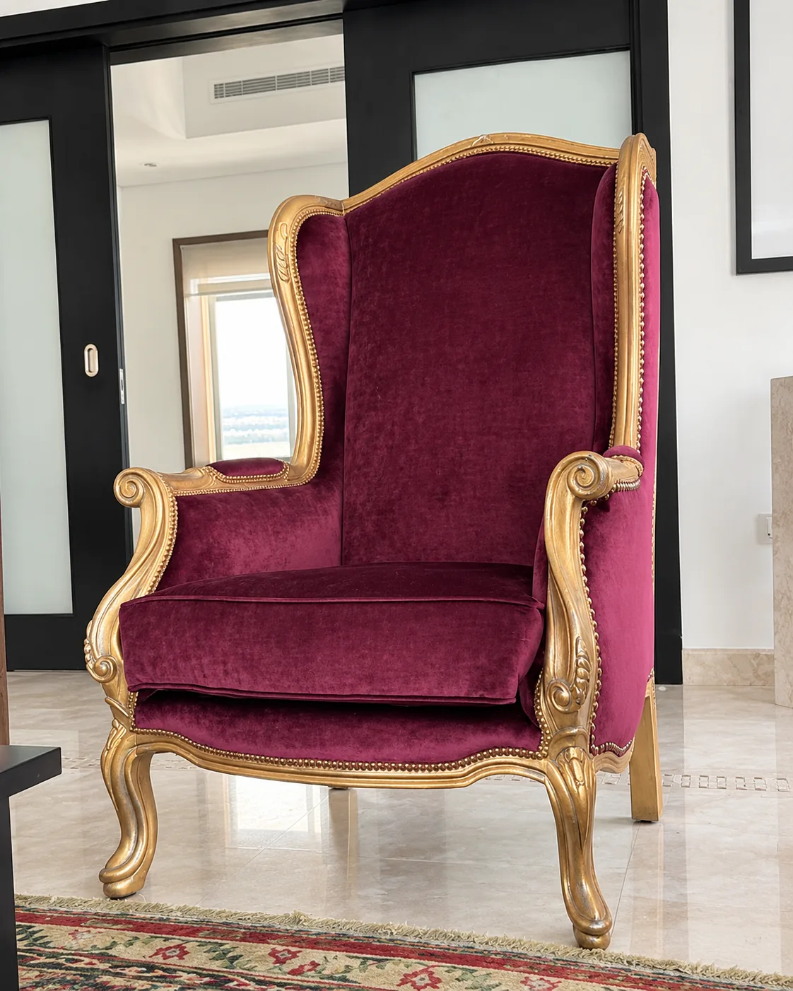 Gilded wingback chair upholstered in burgundy velvet