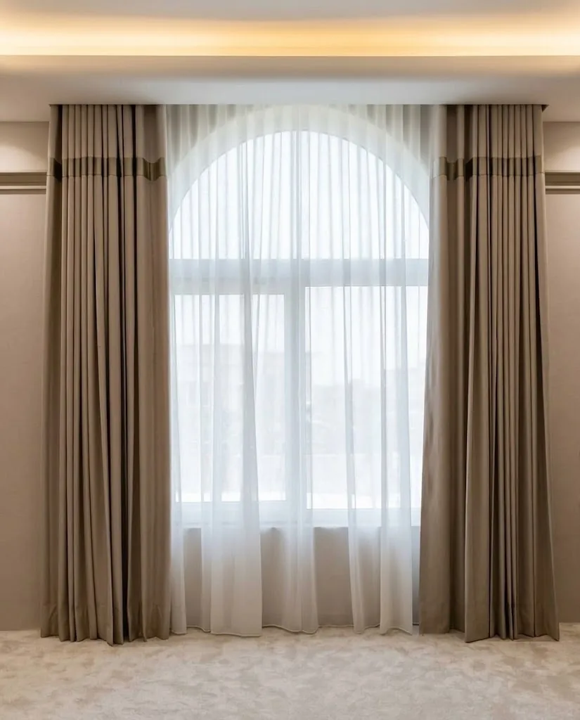 Taupe wave curtains and white sheer on a tall arched window