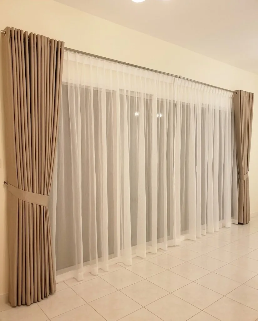 Beige pleated curtain held back with a tie-back over white sheers
