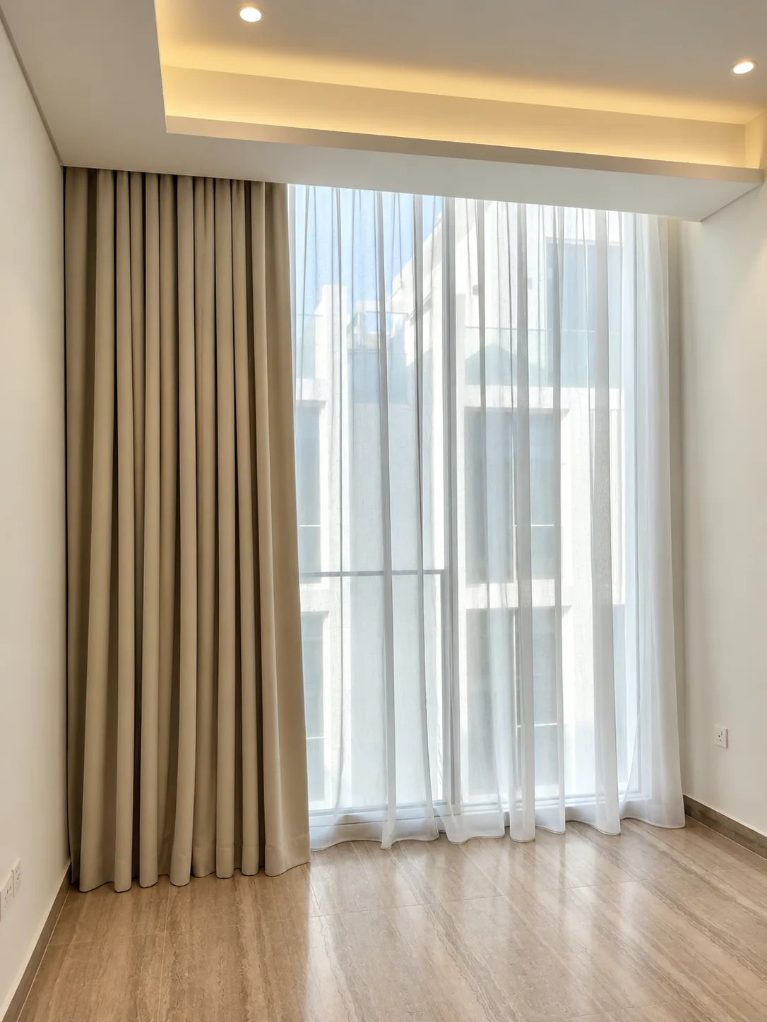 Taupe pleated curtain and white sheer on a floor-to-ceiling window