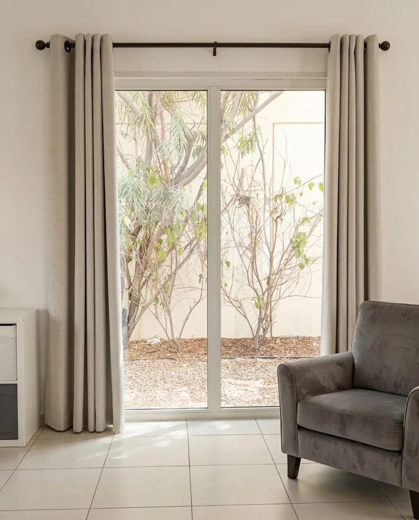 Grey eyelet curtains on a black rod beside living room garden doors