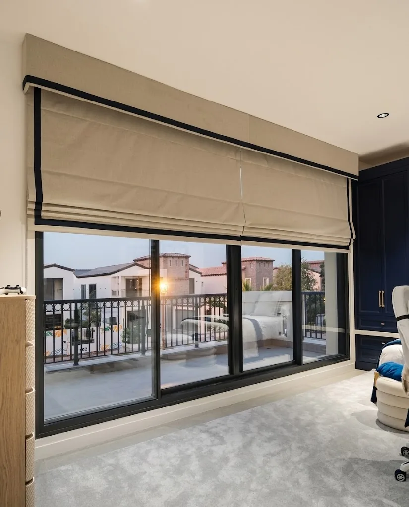 Beige Roman blind with a black border above balcony doors at dusk