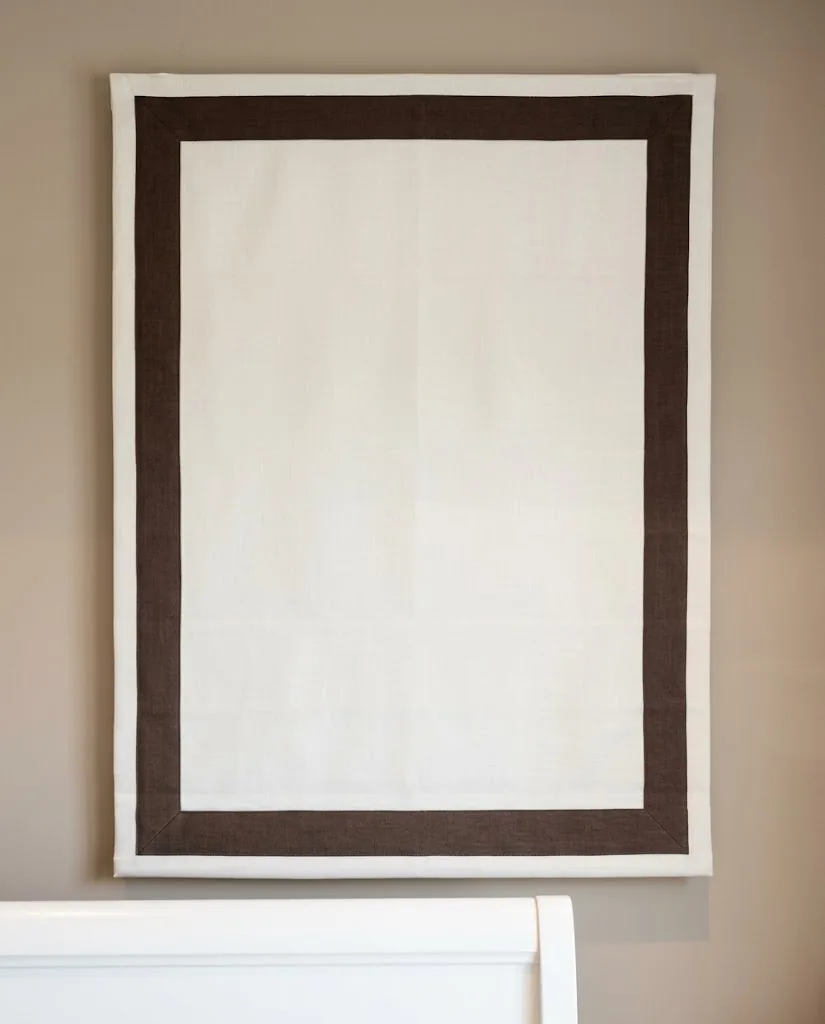 Close-up of a white Roman blind with a brown border