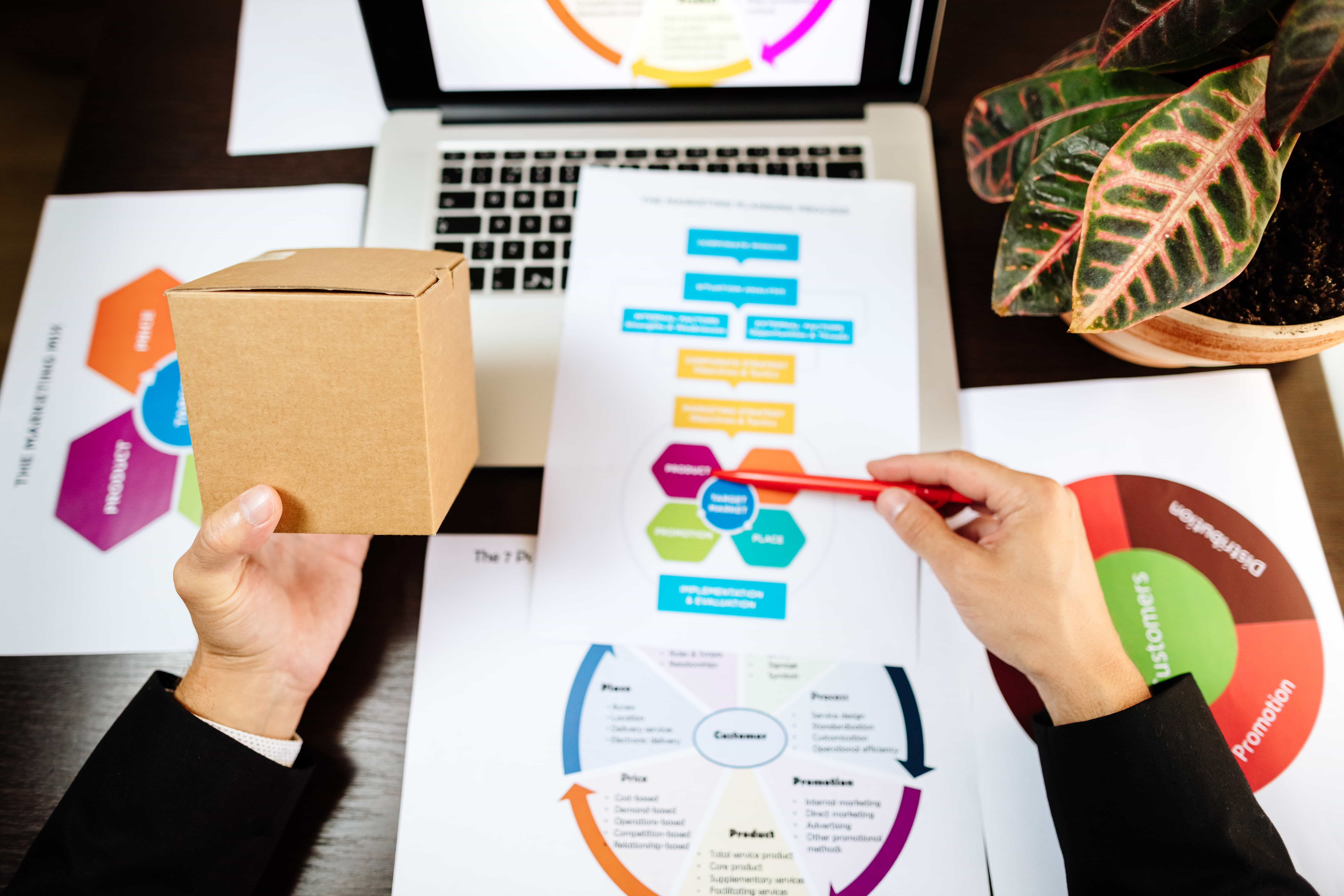 Top-down view of a marketing expert in Chicago, IL, pointing to a strategic planning document next to a laptop and a cardboard product box.