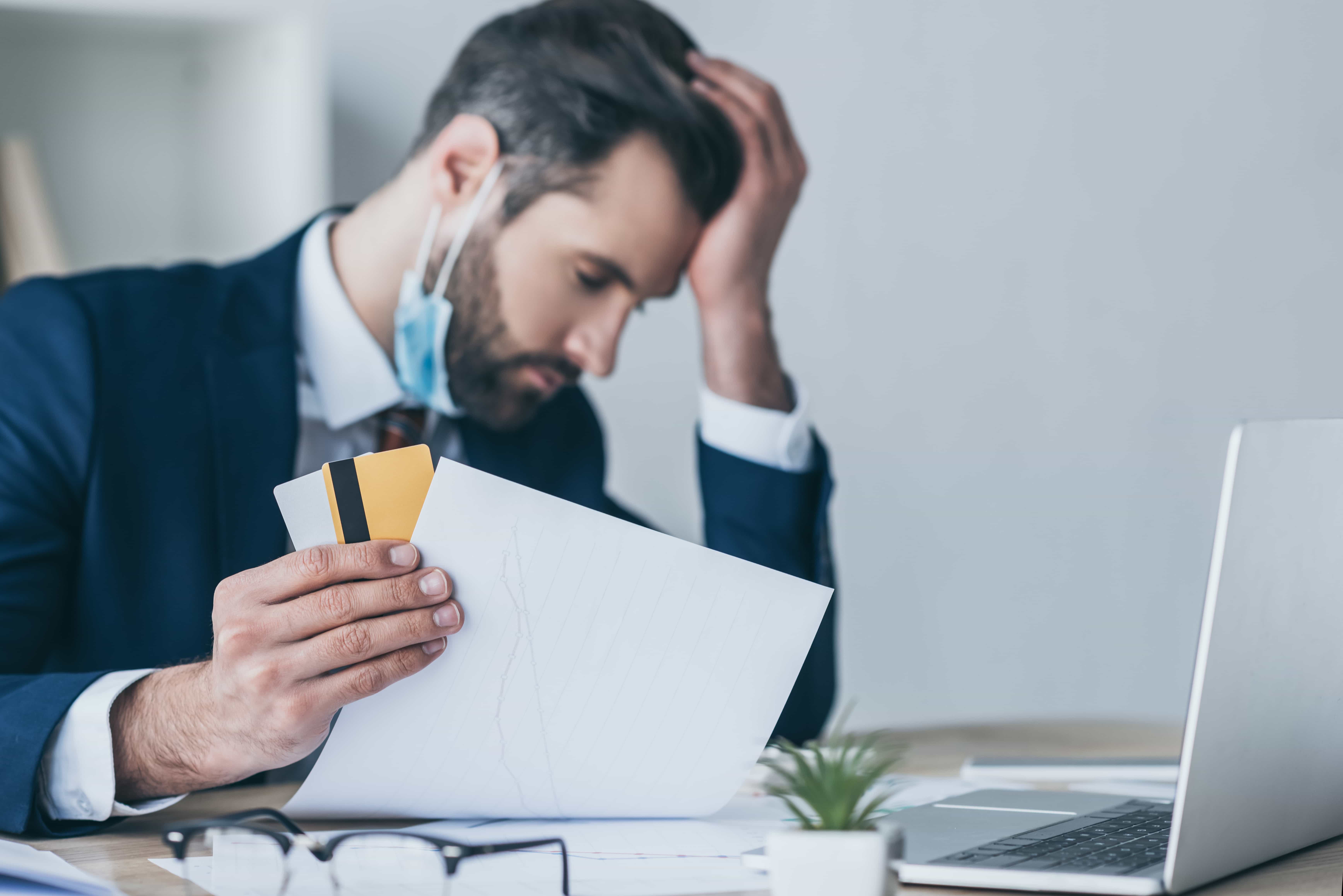 Stressed businessman in a suit reviewing financial documents and credit cards, illustrating the need for professional business debt relief services in Florida.