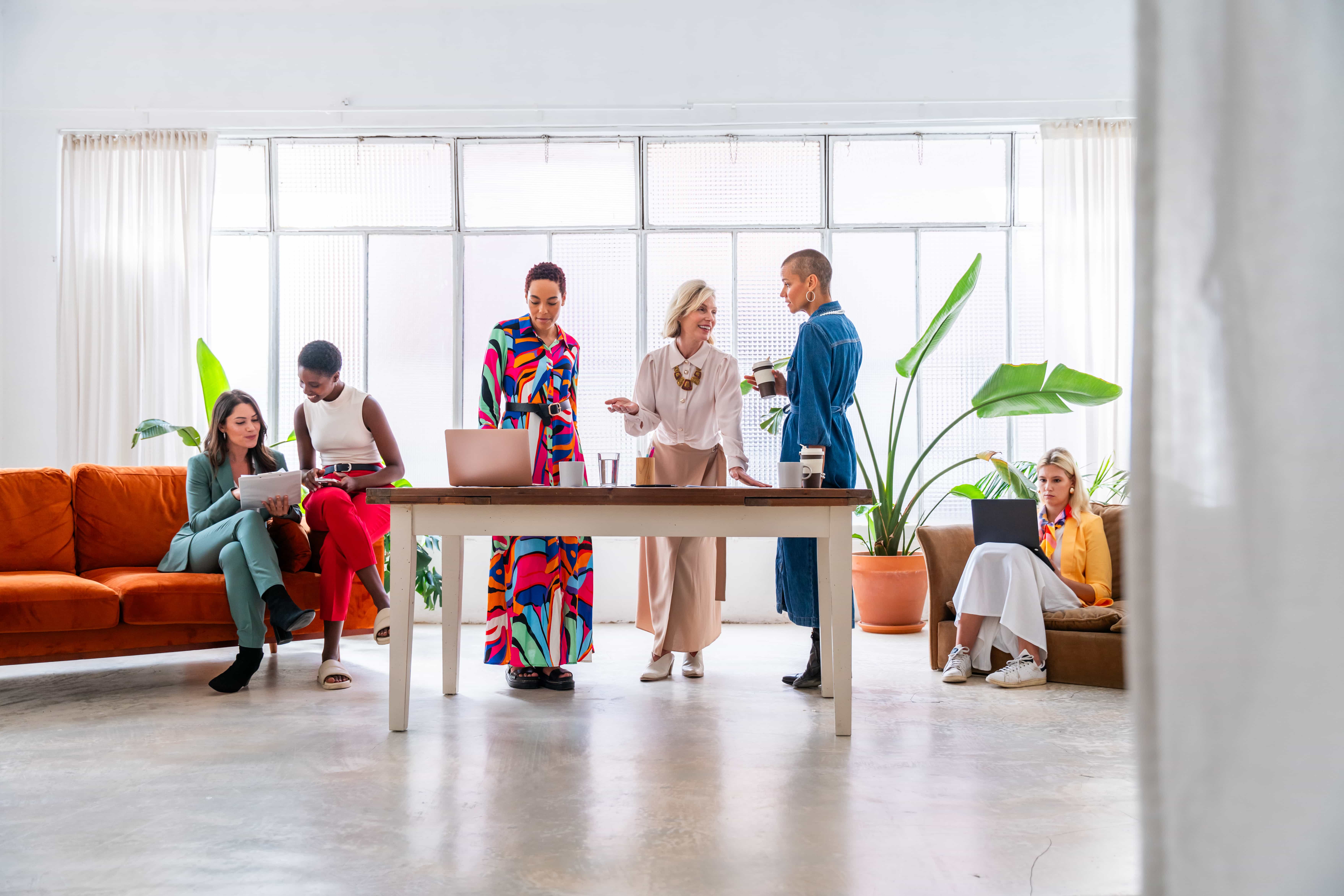 A diverse group of professional women collaborating and networking in a bright, modern coworking space, representing business consulting services in Florida.